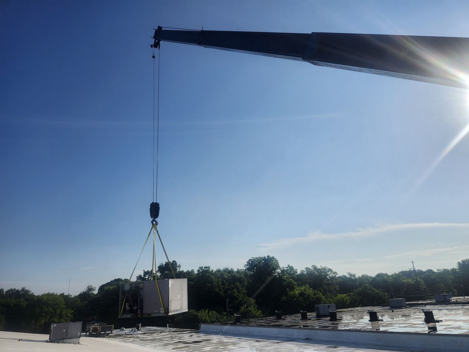Package unit hanging from a crane over a commercial roof