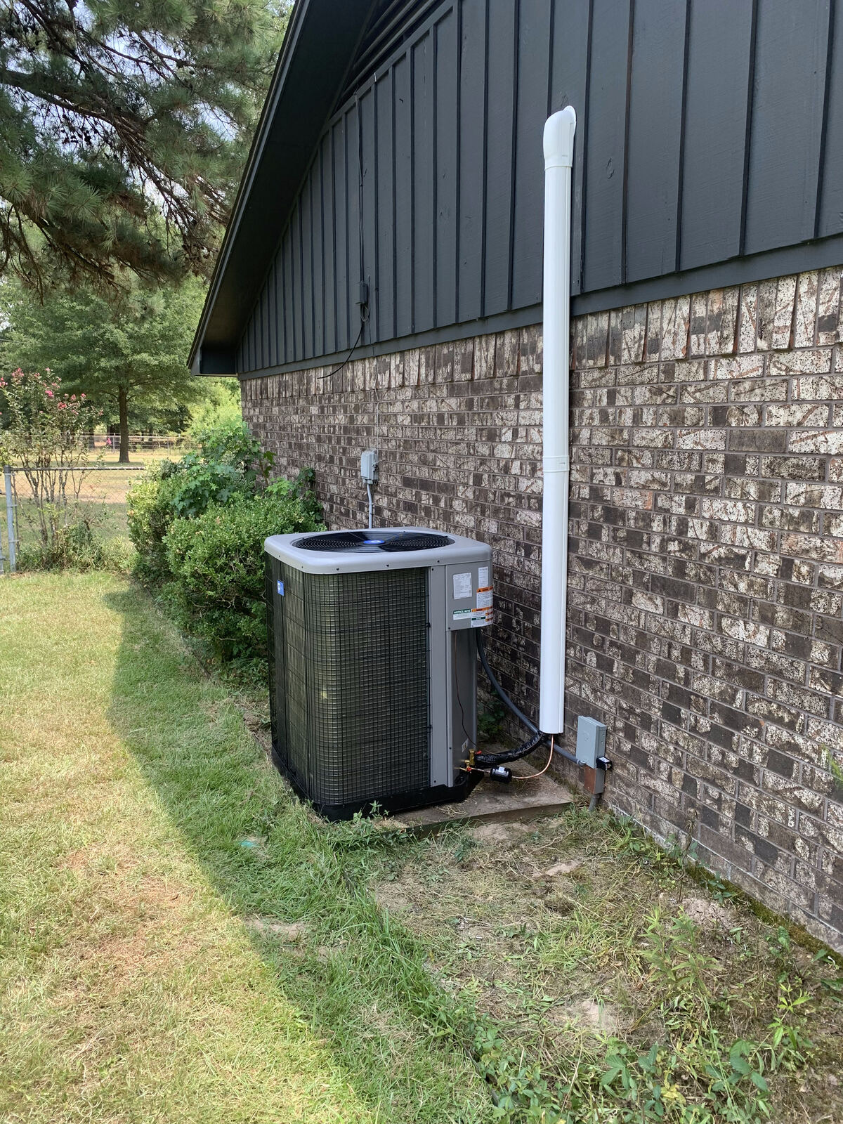 New residential condenser set on a pad against a brick house