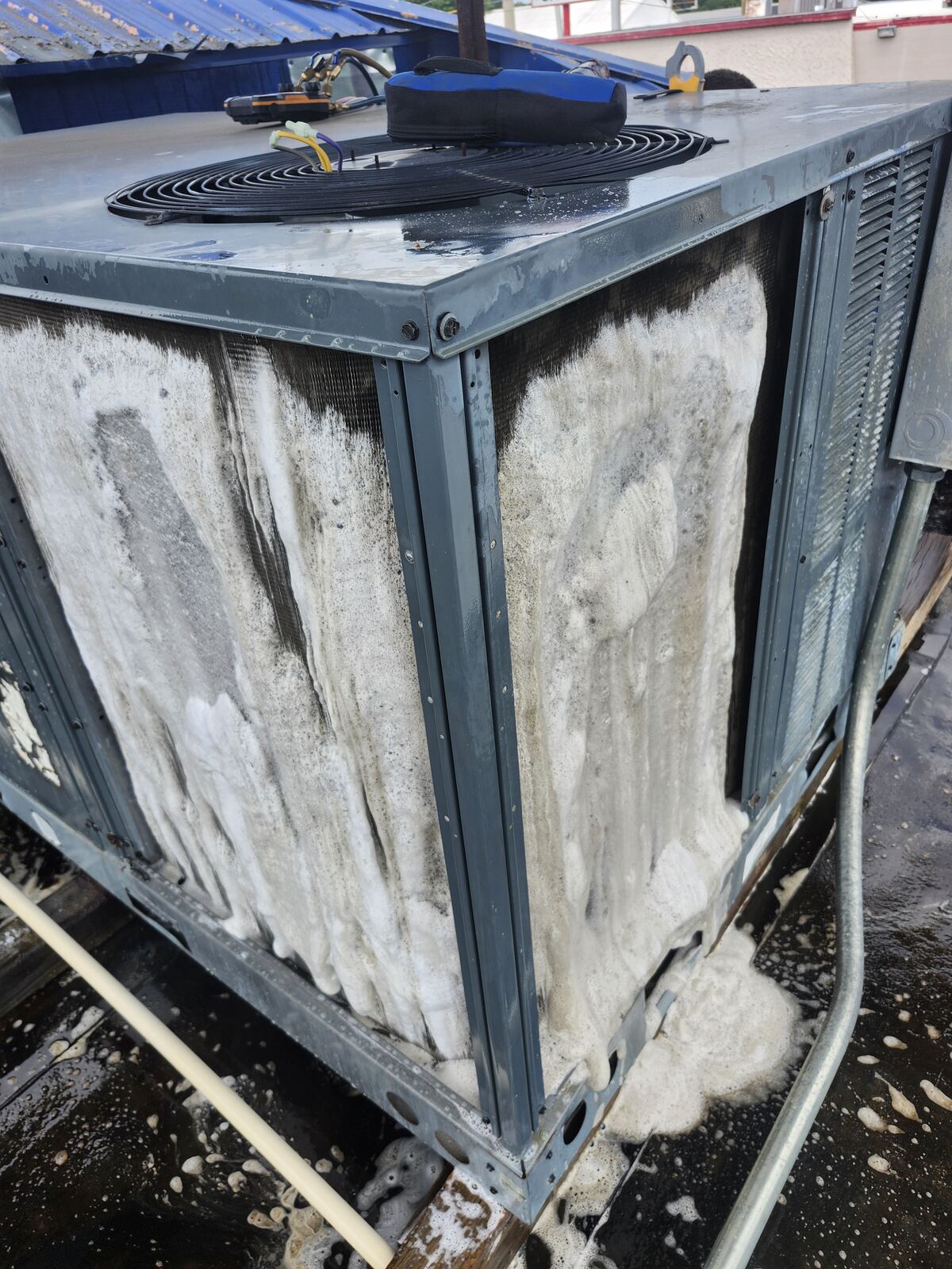 Rooftop condenser coil covered in coil cleaner during a maintenance visit
